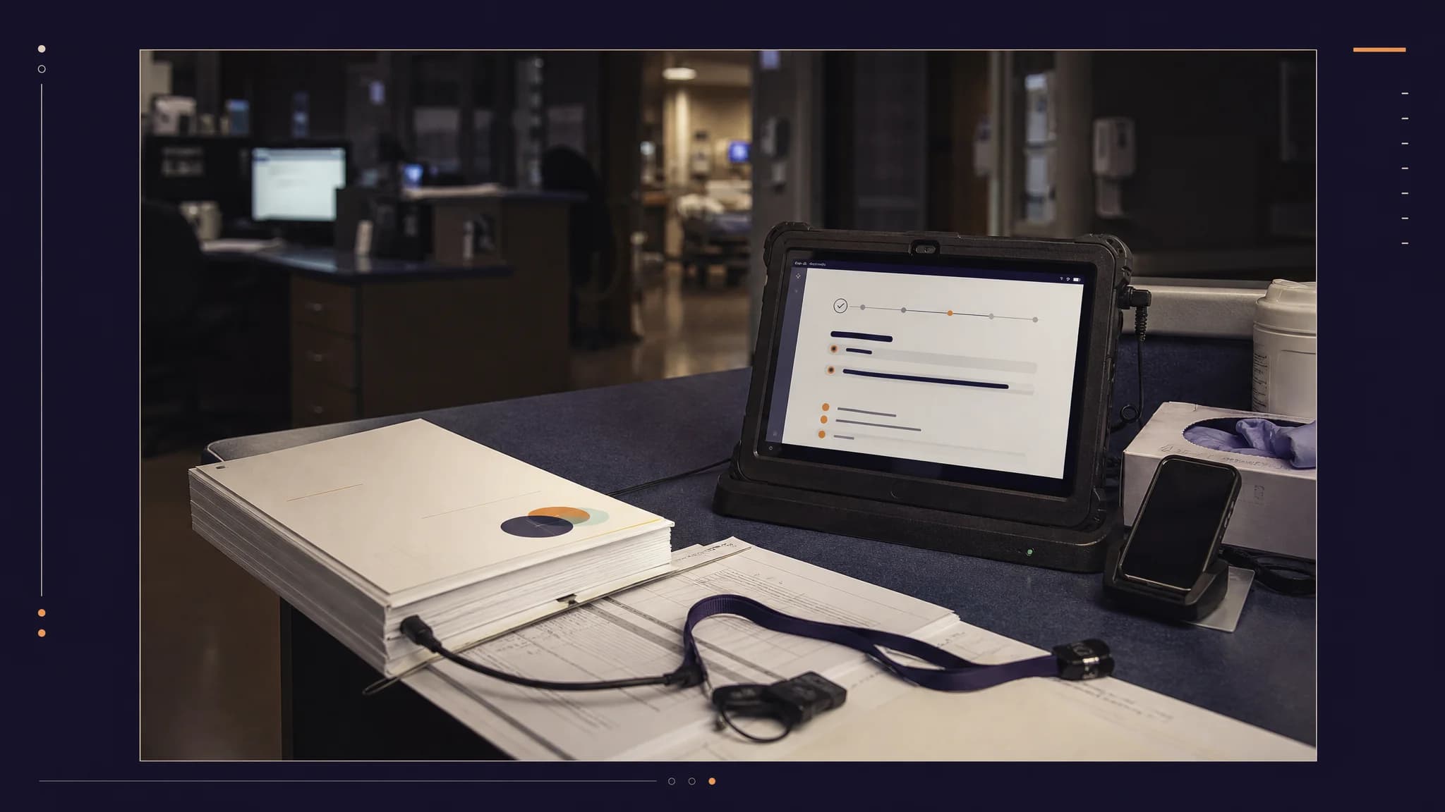 A tablet displays data alongside a stack of papers, a smartphone, and a lanyard on a desk in a dimly lit office.